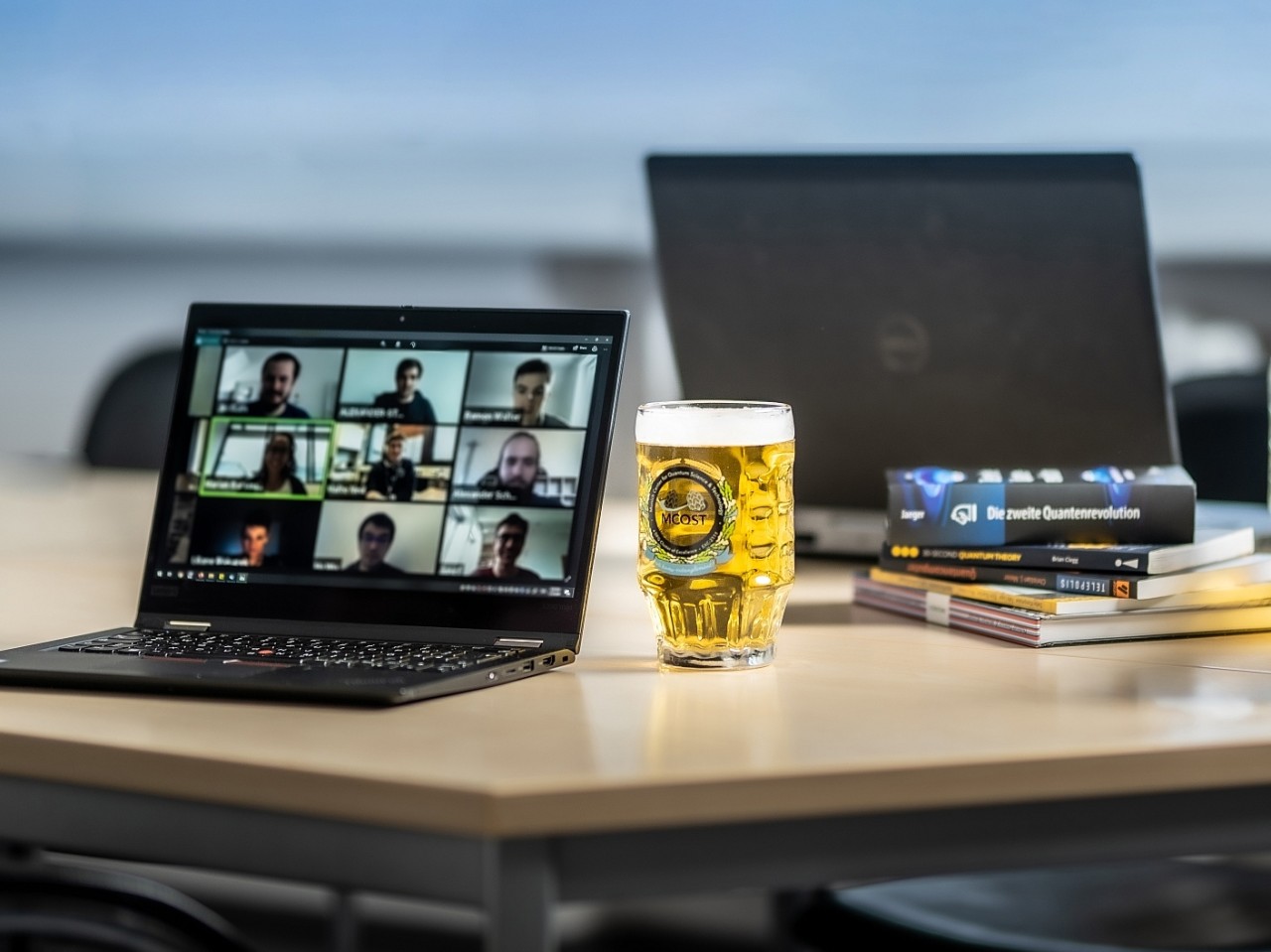 Open laptop with a zoom call on a wooded table with a full bier mug nearby and quantum physics books. 