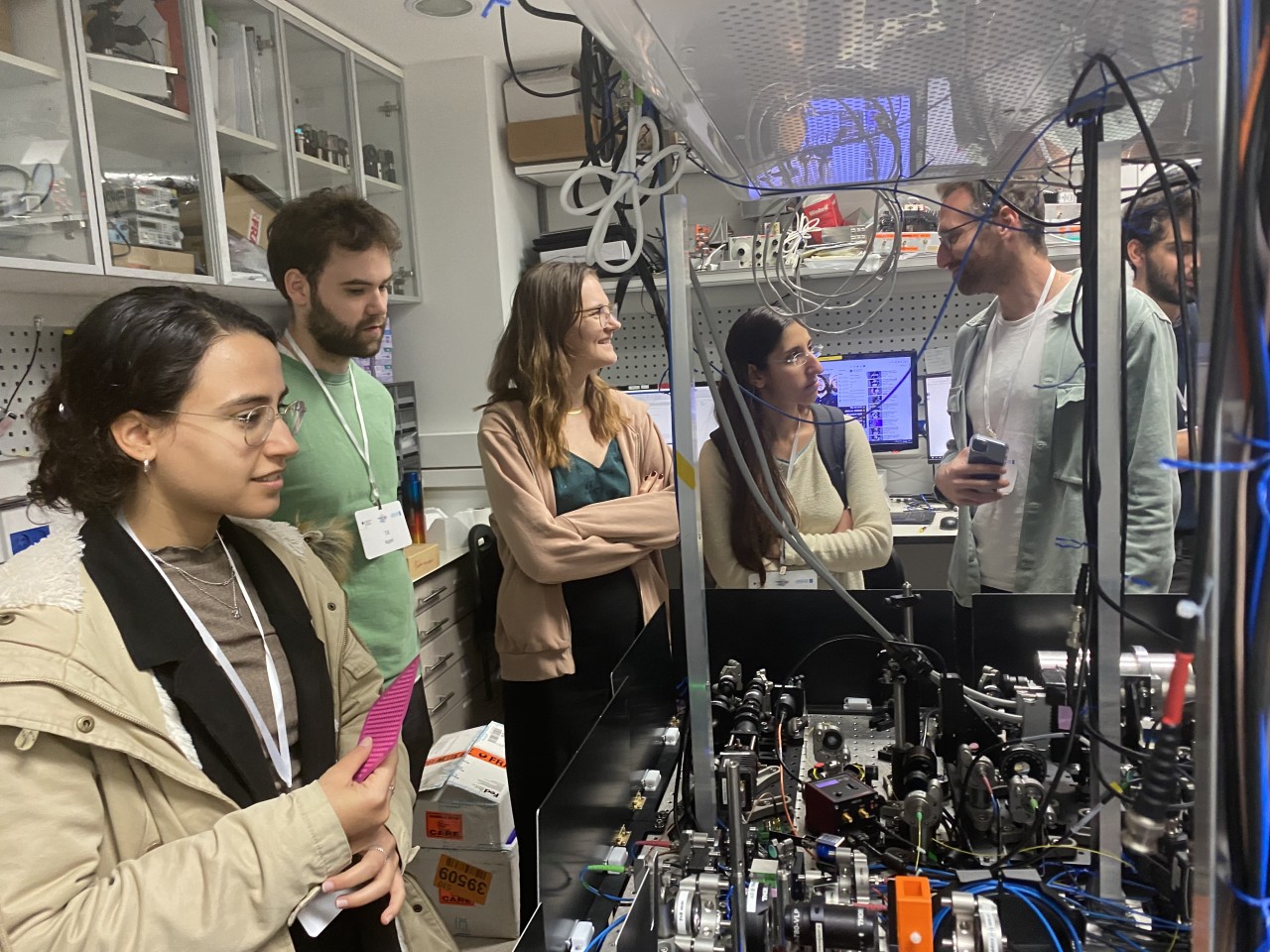 Students visiting a quantum research lab, standing around an optical table. 