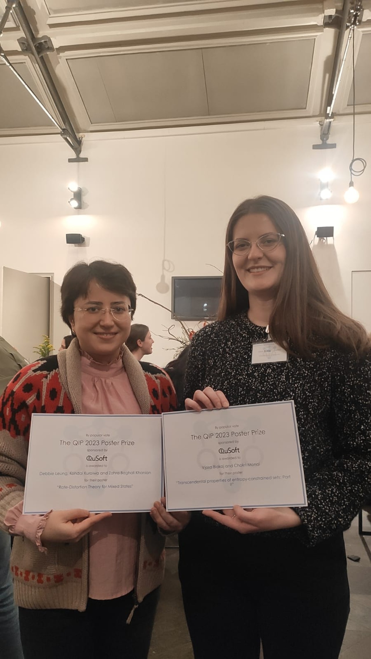 Two female scientists holding a poster award diploma they each one at QIP2023. 