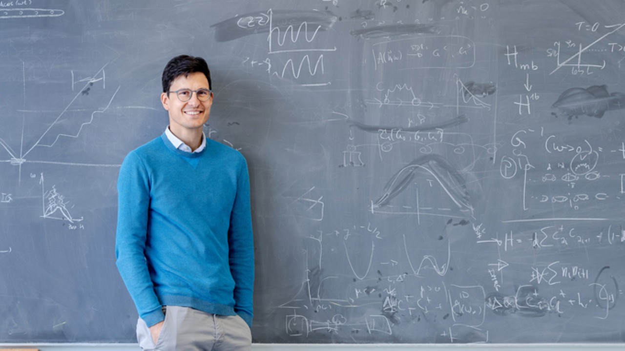 Professor standing in front of a black board filled with formulas.