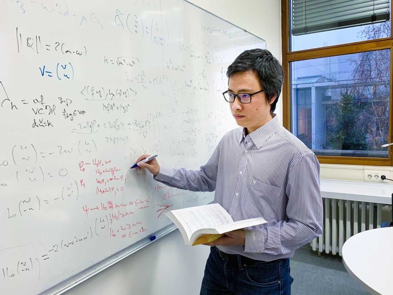 Phan Thành Nam writing mathematical formulas on a whiteboard in his office at LMU Munich.