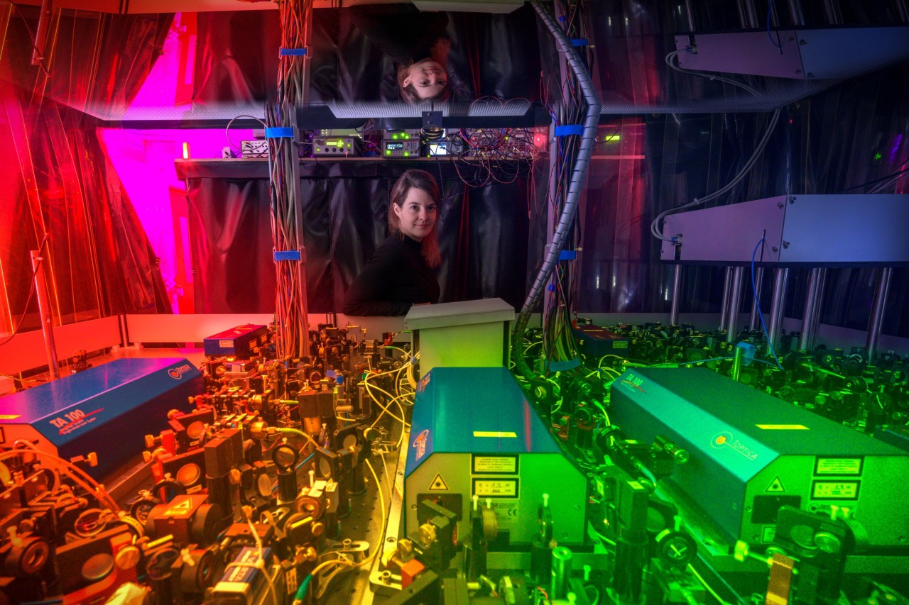 Monika Aidelsburger in one of her labs, standing behind an intricately organized assembly of lenses, mirrors, and lasers.